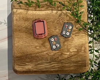 Può includere: Due piccole teglie da forno con una varietà di caramelle e biscotti colorati su un tagliere di legno. Le teglie da forno sono grigie con bordi rossi. Il tagliere è marrone con venature di legno naturale.