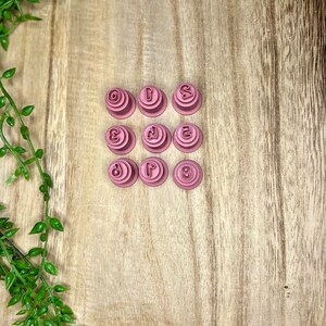 May include: Nine pink plastic number cookie cutters, arranged in a 3x3 grid on a wooden surface. The numbers are 0, 1, 2, 3, 4, 5, 6, 7, and 8.
