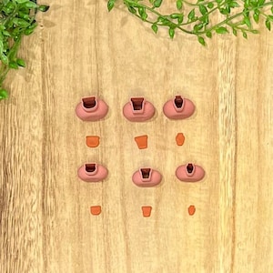 May include: Nine pink silicone earbud tips of various sizes, arranged in three rows on a wooden surface.