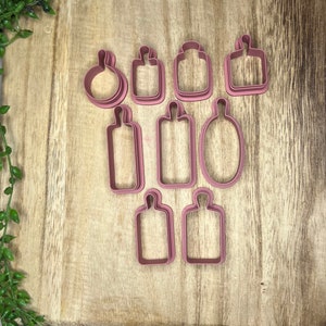 May include: A set of ten pink plastic cookie cutters shaped like bottles and jars. The cutters are arranged in two rows on a wooden surface.