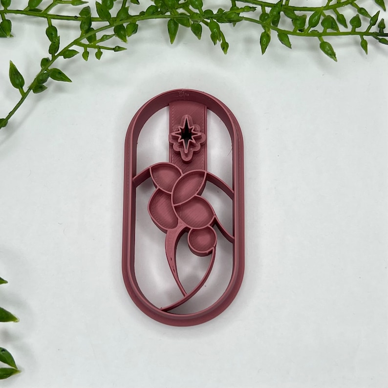May include: A pink plastic cookie cutter shaped like a stained glass window with a star at the top and a floral design at the bottom.