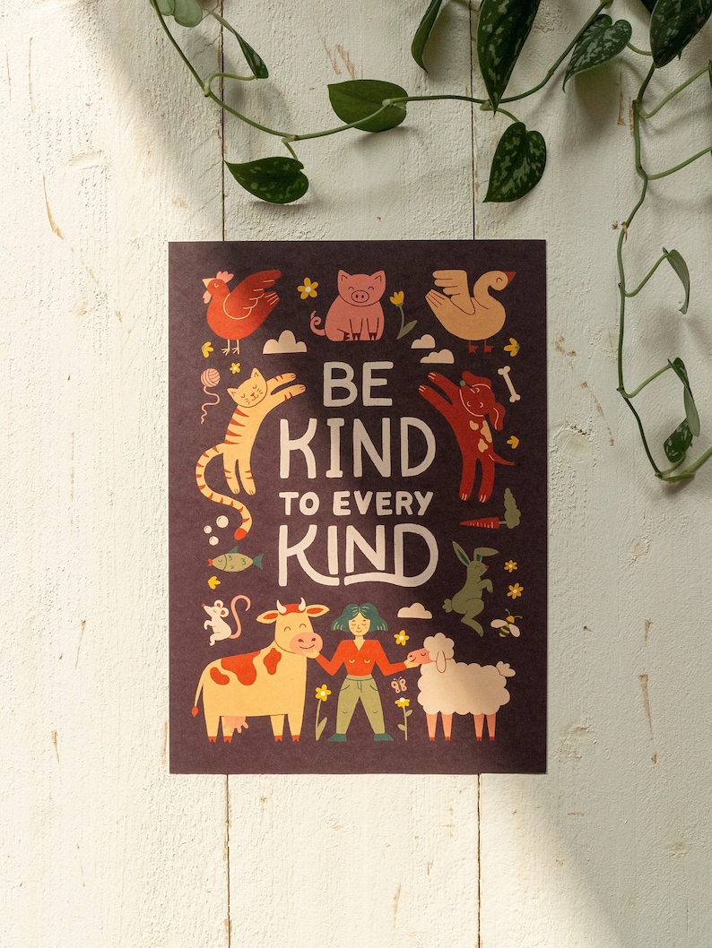 May include: A poster with the text "BE KIND TO EVERY KIND" surrounded by illustrations of various animals, including a chicken, pig, cat, dog, cow, sheep, and rabbit. The poster has a dark brown background with a white wooden surface in the background.