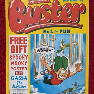 Op de afbeelding: Een gele en rode comicboekomslag met de titel "Buster" en de tekst "No 1 for FUN". De omslag toont een cartoonfiguur die uit de lucht valt met de tekst "WATCH OUT BELOWWW!" en een gratis cadeau-aanbieding voor een "Spooky Wooky Poster".