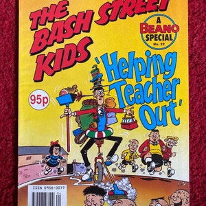 Pode incluir: Uma capa de banda desenhada Beano Special com os Bash Street Kids. A capa é amarela com texto vermelho e azul. O título é "The Bash Street Kids" e o subtítulo é "Helping Teacher Out". A capa apresenta uma ilustração de banda desenhada de um rapaz a andar de monociclo com uma grande mochila às costas. Existem outras personagens de banda desenhada na capa, incluindo uma rapariga com um laço vermelho no cabelo e um rapaz com uma camisa de riscas vermelhas e brancas.
