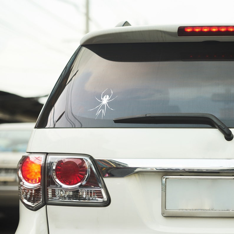 May include: A white SUV with a spider graphic sticker on the rear window. The car has a rear license plate, a rear wiper, and red taillights.