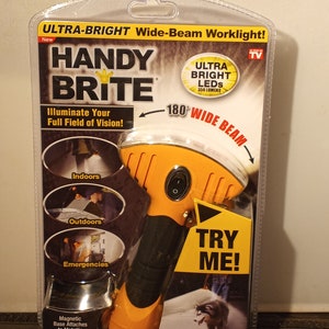 May include: Orange and black Handy Brite worklight in packaging. The package highlights the ultra-bright wide beam, 350 lumens, and 180-degree beam. Features include a magnetic base, impact resistance, and a non-slip comfort grip. The packaging says "Try Me!"