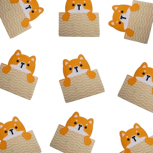 Puede incluir: Un conjunto de nueve clutches bordadas de color naranja y blanco con un perro Shiba Inu asomando por la parte superior de cada clutch.