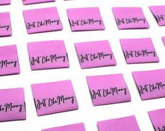 May include: A collection of pink fabric labels with the text "Just Like Mummy" printed in black.