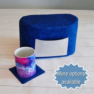 May include: A blue fabric cover with a white pocket for a small appliance, like a toaster or coffee maker. A blue coaster with a pink and white mug sits on a white surface. The text "More options available" is in a blue starburst.