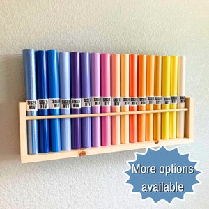 May include: A wooden shelf with 20 rolls of heat transfer vinyl in various colors, including blue, purple, pink, orange, yellow, and green. The rolls are labeled "Siser HTV".