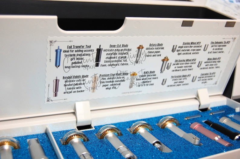Peut inclure: Un coffret en plastique blanc avec un int&eacute;rieur bleu, contenant un ensemble de huit lames de coupe diff&eacute;rentes pour une machine de loisirs cr&eacute;atifs. Les lames sont &eacute;tiquet&eacute;es avec leurs utilisations, telles que "Outil de transfert de feuille", "Lame de d&eacute;coupe profonde", "Lame rotative", "Lame pour tissu coll&eacute;", "Lame de pr&eacute;cision fine", "Lame de couteau", "Roue de pointage n&deg; 21" et "Bande adh&eacute;sive fine n&deg; 21".