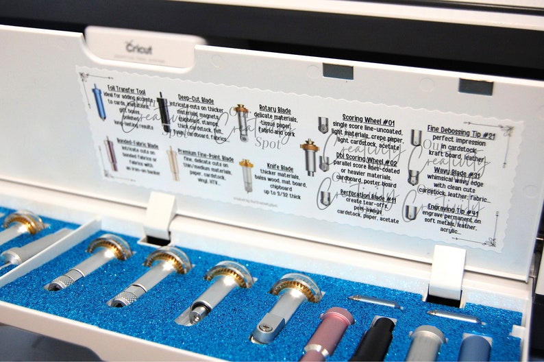 Peut inclure: Gros plan sur une machine Cricut blanche avec un insert en mousse bleue. La machine est ouverte et l'insert contient divers outils, dont une roue &agrave; rainurer, une pointe de gaufrage fine, une lame ondul&eacute;e et une pointe de gravure. Les outils sont &eacute;tiquet&eacute;s avec leurs noms et descriptions.