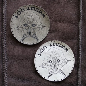 May include: Two white leather round patches with black stitching and a black and white illustration of a robot head with the text "VIVE LA COC" on each patch.