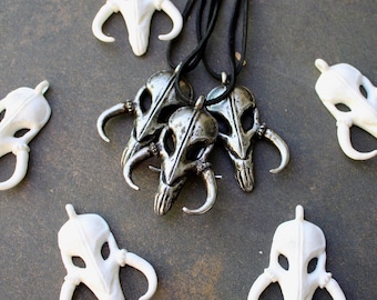 May include: Five silver Mandalorian skull pendants on black cords. Four of the pendants are white and one is silver.