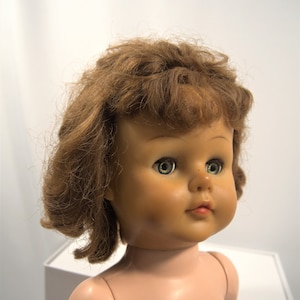 Op de afbeelding: Een vintage pop met bruin haar en groene ogen. De pop is naakt en heeft een geschilderd gezicht.