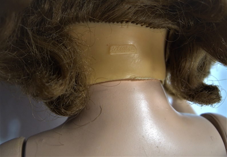Op de afbeelding: Close-up van de achterkant van een poppenhoofd met bruin haar. De nek van de pop heeft een markering met de tekst "Dollcraft".