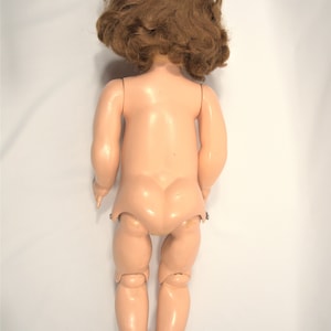 Op de afbeelding: Een vintage porseleinen pop met bruin krullend haar en een naakt lichaam. De pop heeft scharnierende armen en benen.