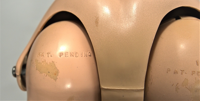 Op de afbeelding: Close-up van een schoudergewricht van een vintage pop met de tekst "PAT. PENDING" in reli&euml;f op de kunststof.