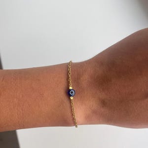Könnte beinhalten: Ein goldenes Kettenarmband mit einem blauen Glücksbringer.