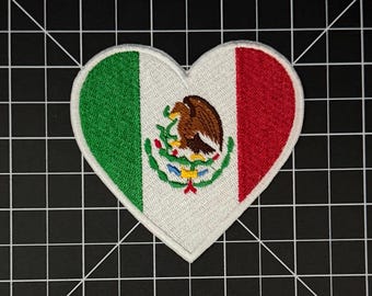 May include: A heart-shaped embroidered patch featuring the flag of Mexico. The design includes vertical green, white, and red stripes with the central Mexican coat of arms depicting an eagle perched on a cactus, surrounded by a green wreath.