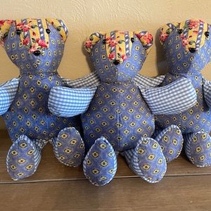 Puede incluir: Tres osos de peluche hechos a mano con patchwork de tela con estampado azul y amarillo. Los osos están sentados sobre una superficie de madera.