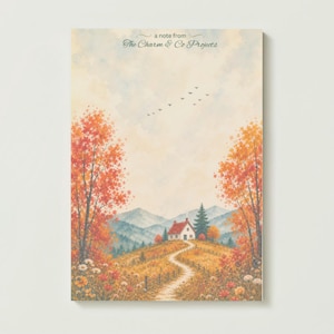 May include: A rectangular notepad featuring a watercolour landscape of a small house on a hill with a winding path, surrounded by autumn trees in shades of orange and red, with the text "a note from The Charm & Co Projects" at the top.