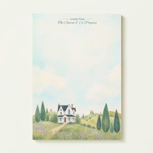 May include: A rectangular notepad featuring a watercolour illustration of a white house with a dark roof and red door, set in a rolling green landscape with tall cypress trees and wildflowers under a pale blue sky with the text a note from The Charm & Co Projects.