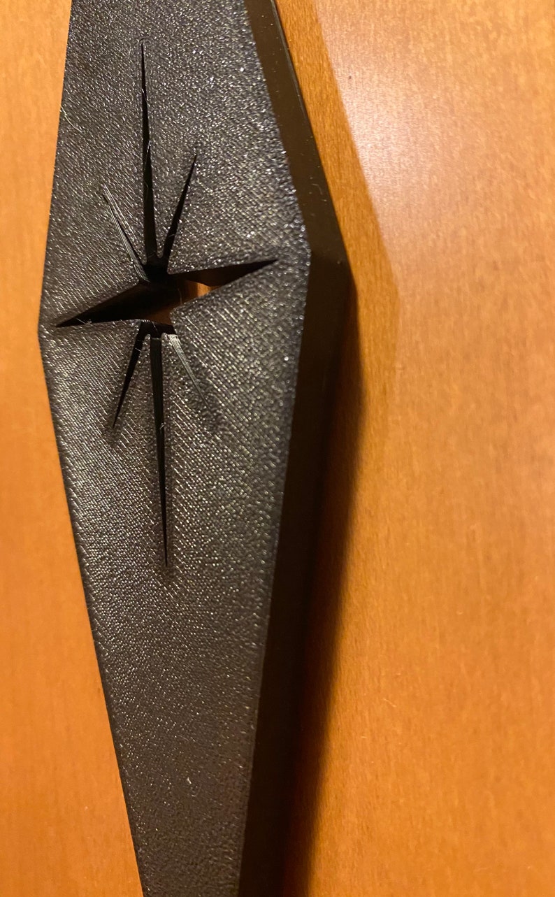 May include: A black diamond-shaped ornament with a cut-out star design. The ornament has a textured surface.