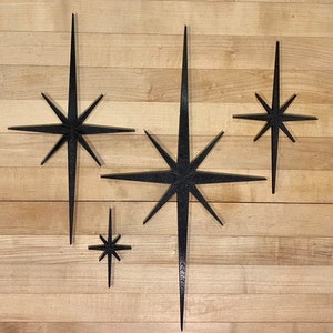 May include: Four black starburst shapes of varying sizes are arranged on a woodgrain surface. The largest starburst is in the center of the image, with the other three stars arranged around it.