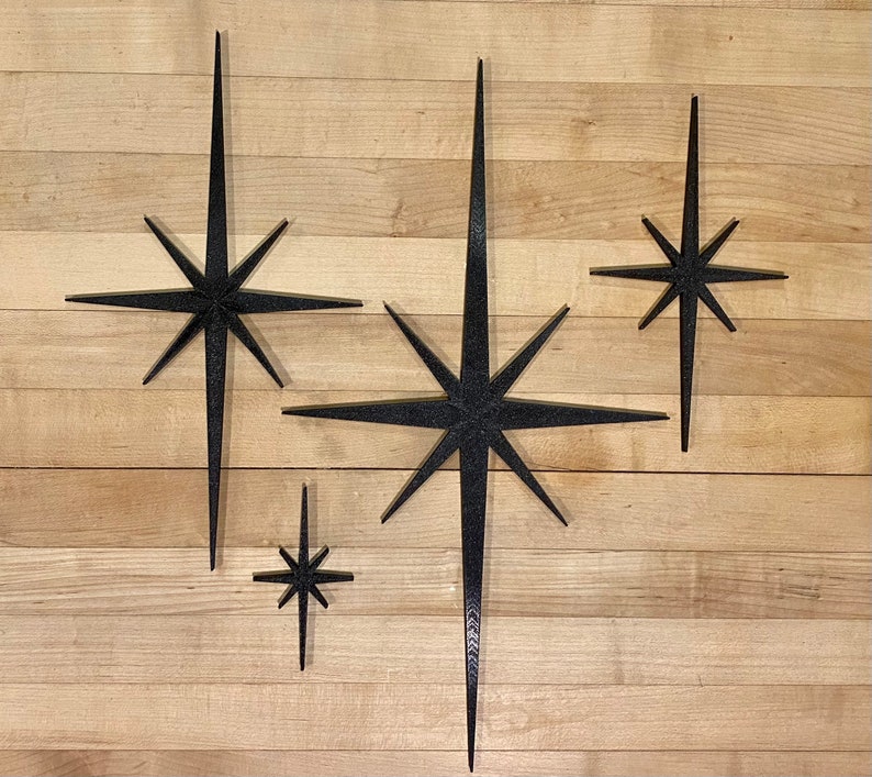 May include: Four black starburst shapes of varying sizes are arranged on a woodgrain surface. The largest starburst is in the center of the image, with the other three stars arranged around it.