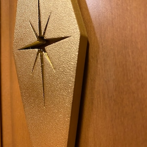 May include: A gold-colored, diamond-shaped door handle with a star-shaped cutout in the center.
