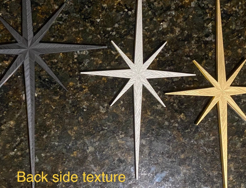 May include: Three decorative star-shaped ornaments in black, silver, and gold. The stars have a textured surface and a pointed design.