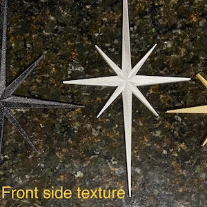 May include: Three decorative star ornaments in black, silver, and gold. The stars have a textured, sparkly finish.  Front side texture.
