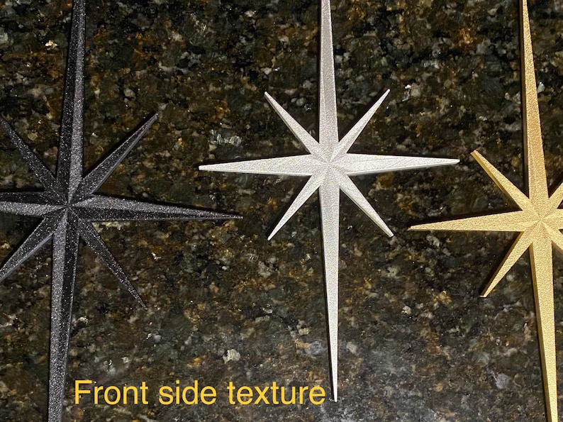 May include: Three decorative star ornaments in black, silver, and gold. The stars have a textured, sparkly finish.  Front side texture.
