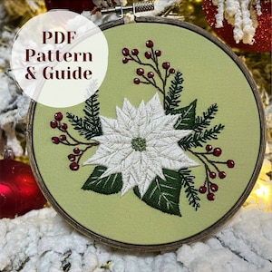 May include: A white poinsettia flower with green leaves and red berries embroidered on a light green fabric in a wooden embroidery hoop.  PDF Pattern & Guide.
