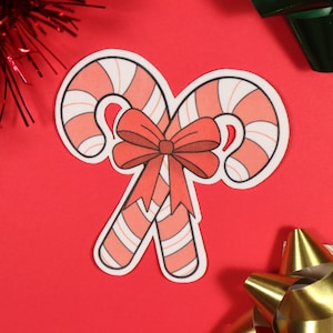 May include: Two red and white candy canes tied together with a red bow. The candy canes are on a red background.