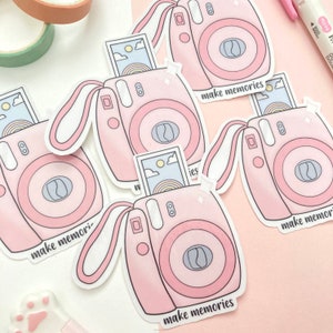 May include: Four pink and white instant camera stickers with the text "make memories" on each. The stickers are on a pink background.