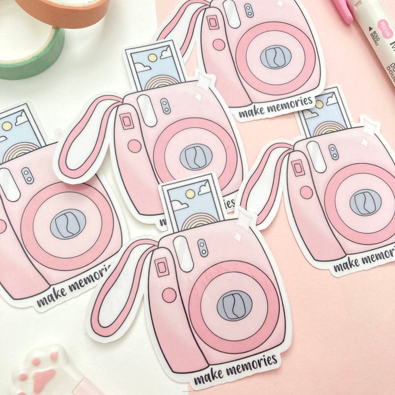 May include: Four pink and white instant camera stickers with the text "make memories" on each. The stickers are on a pink background.