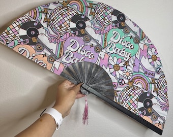May include: A black and white hand fan with a colourful design featuring the text "Disco Baby" and "Disco Bat". The fan has a pink tassel.