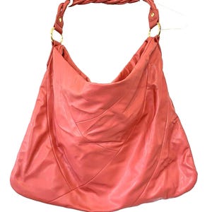 May include: A coral-colored leather hobo bag with a braided strap and gold-tone hardware. The bag has a large, slouchy design with stitched details. The strap is attached to the bag with gold rings.