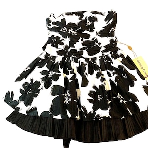 May include: A strapless dress with a black and white floral design. The dress has a pleated hem and a tag that reads "Dancing C...ee". The dress is made of a light fabric, suitable for warmer weather.