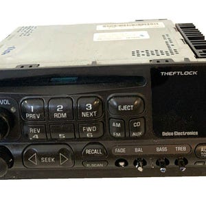 Peut inclure: Un autoradio noir Delco Electronics comprenant une fente pour lecteur CD, une zone d'affichage numérique marquée THEFTLOCK, ainsi que des boutons physiques pour le volume, la syntonisation, la recherche, l'éjection et les réglages audio.