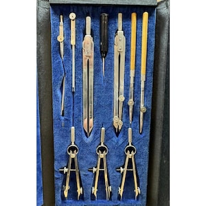 May include: A vintage drafting set with various metal and wood tools, including compasses, dividers, and a stylus, arranged in a blue velvet-lined case. The tools are silver and gold-toned, with wooden handles.