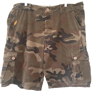 Könnte beinhalten: Tarnfarbene Cargo-Shorts in Braun-, Grün- und Schwarztönen. Die Shorts haben zwei Vordertaschen, zwei Cargotaschen mit Knopfverschluss sowie einen Knopf- und Reißverschluss. Die Shorts hängen an einem weißen Kleiderbügel.