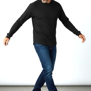 May include: A person wearing a black long-sleeved shirt and blue jeans. The person is also wearing white sneakers. The outfit is casual and comfortable, suitable for everyday wear. The background is plain white.
