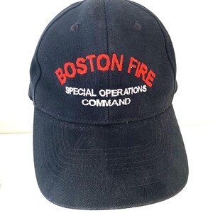 May include: A navy blue baseball cap featuring the embroidered text "BOSTON FIRE" in red. Beneath, in white, it reads "SPECIAL OPERATIONS COMMAND". The cap has a curved peak and a structured crown.