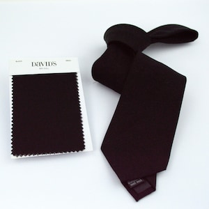 May include: A black necktie and a matching fabric swatch on a white card. The card features the text David's Bridal, the word Black, and the word Mesh. The necktie has a pointed end and a label on the back that reads Hand Made.