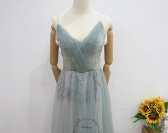 Puede incluir: Un vestido maxi de tul azul claro con escote en V y tirantes finos. El vestido tiene un delicado estampado floral y una falda fluida. El vestido se muestra en un maniquí.
