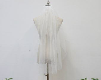 May include: A white tulle bridal veil on a white mannequin. The veil is single-tiered and has a scalloped edge.
