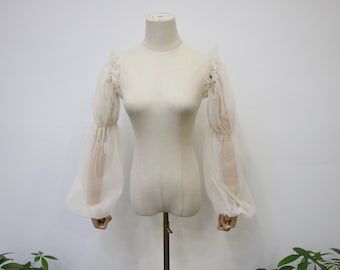 May include: A white sheer blouse with long, gathered sleeves and a ruffled neckline.